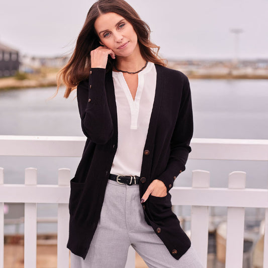 Woman wearing a cashmere black cardigan over a white shirt with gray pants, standing by a white picket fence.