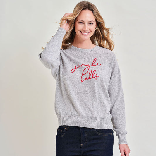 Woman wearing a gray sweater with 'jingle bells' text on a plain background