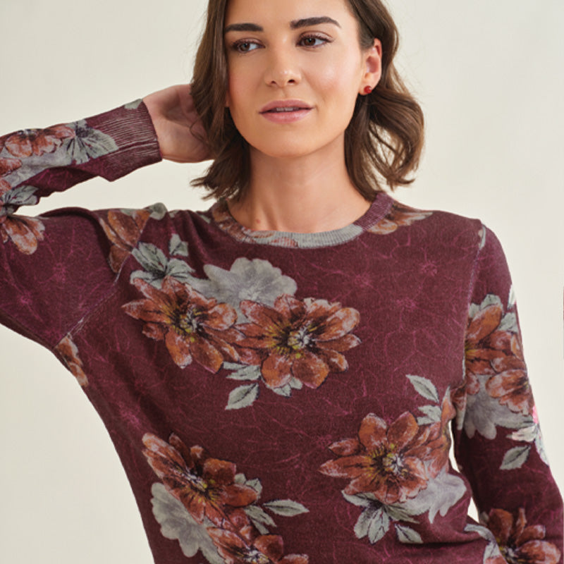 Woman wearing a Cashmere maroon floral sweater against a plain background