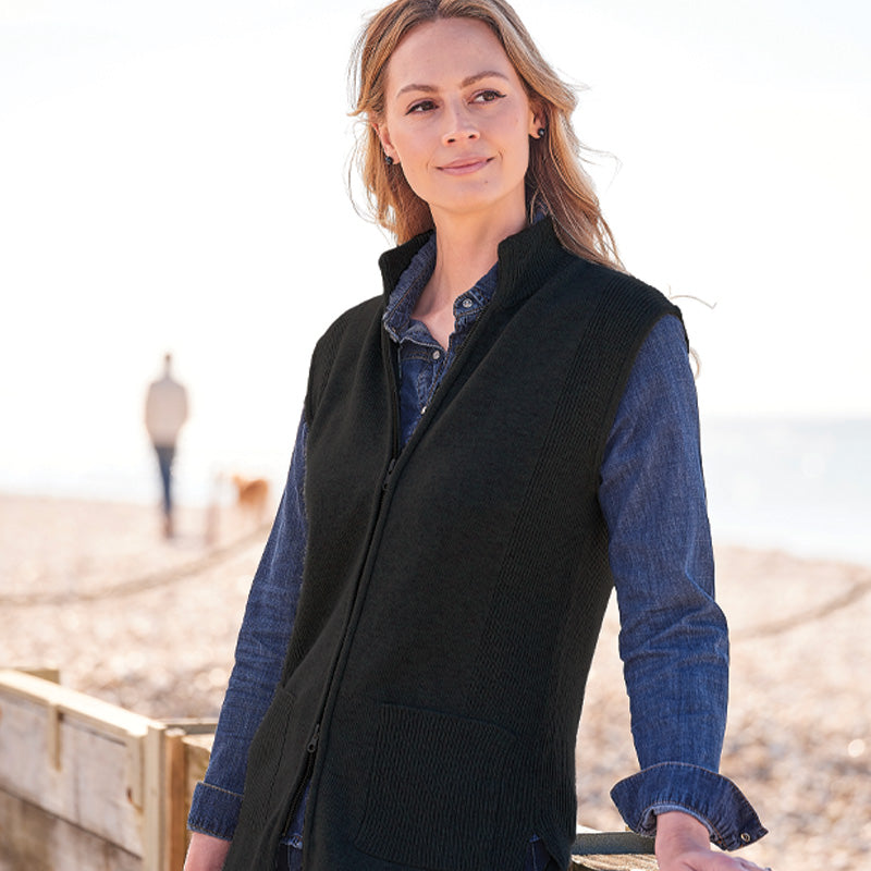 Woman wearing a black cashmere gilet over a blue shirt on a beach.