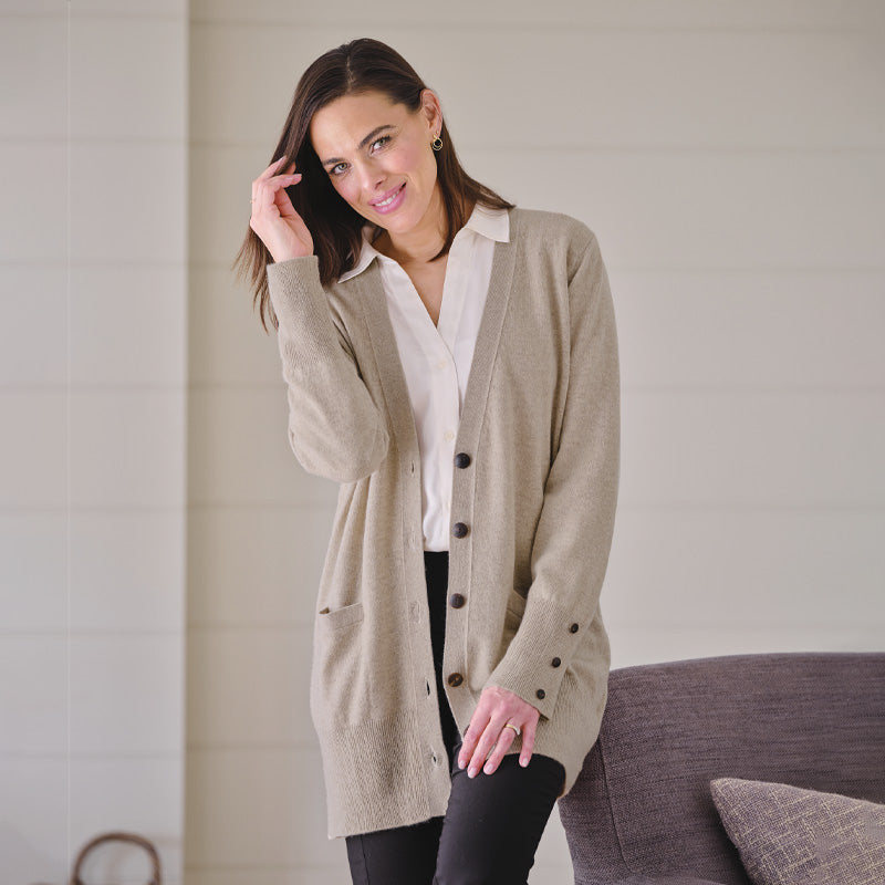 Woman wearing a beige cashmere cardigan over a white shirt in a neutral setting