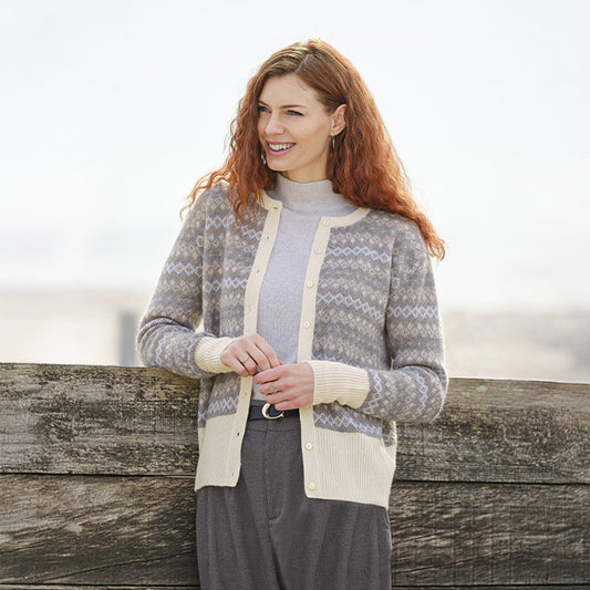 Woman wearing a grey and beige cashmere patterned cardigan standing against a wooden fence with a light background