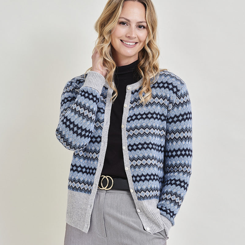 Woman wearing a blues and grey cashmere patterned cardigan standing against a wooden fence with a light background