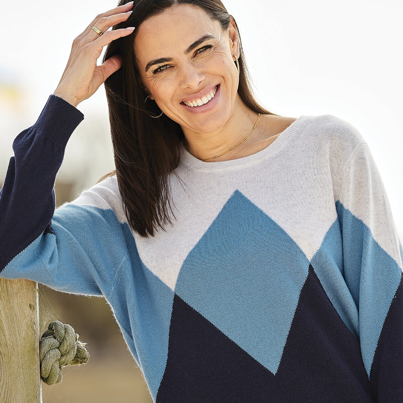 Woman wearing a cashmere diamond blue and white diamond patterned sweater, smiling outdoors.