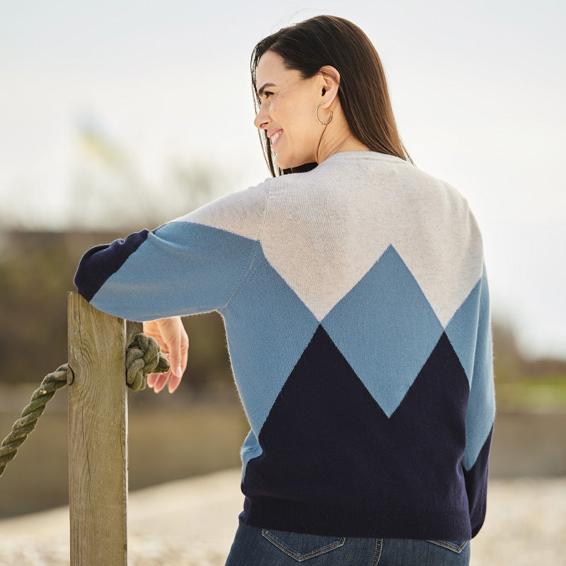 Woman wearing a cashmere blue and white patterned sweater standing by a wooden post outdoors.
