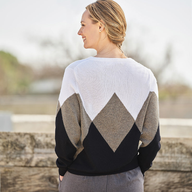 Woman wearing a beige, white and black cashmere diamond-patterned sweater standing outdoors with a blurred background