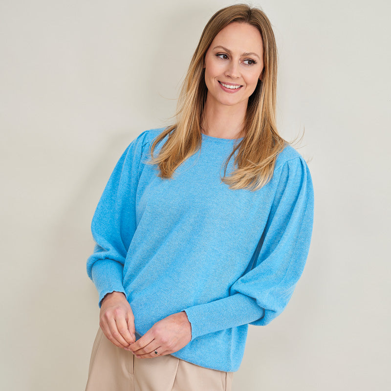 Woman wearing a blue cashmere sweater against a plain background
