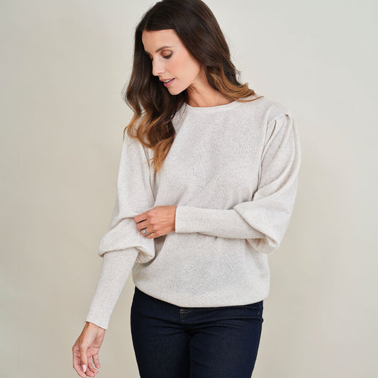 Woman wearing a light cream cashmere sweater against a plain background