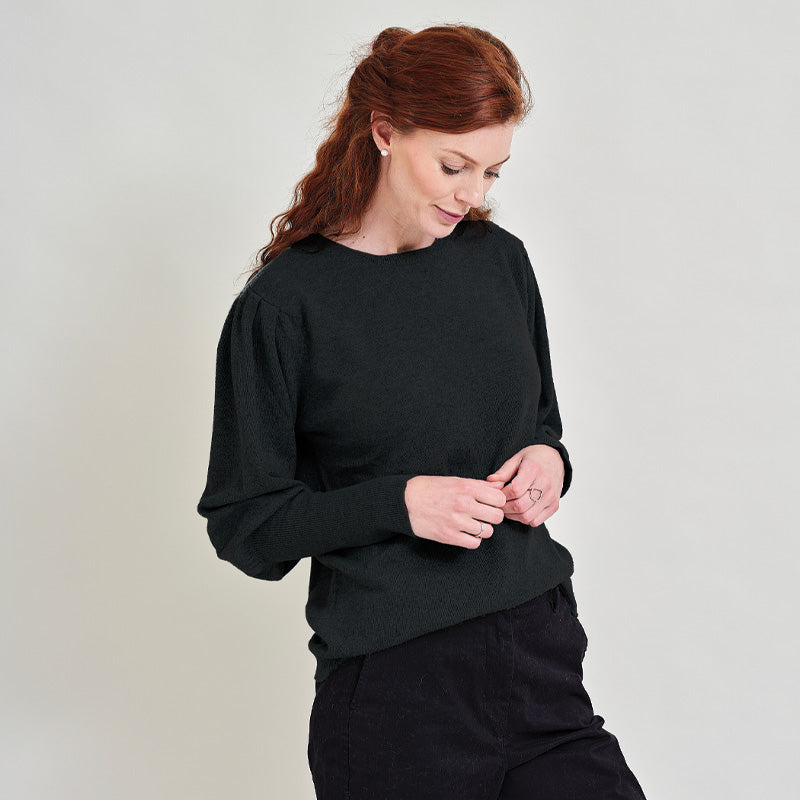 Woman wearing a black cashmere sweater and pants against a plain background