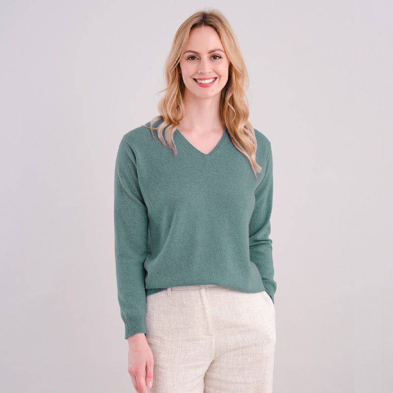Woman wearing a green sweater and white pants against a plain background