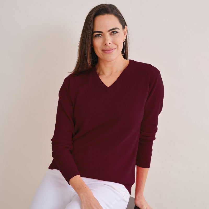 Woman wearing a burgundy sweater and white pants against a plain background