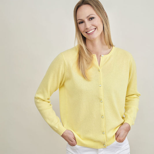 Woman wearing a cashmere yellow cardigan against a plain background