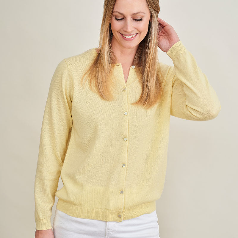 Woman wearing a yellow cashmere cardigan against a plain background