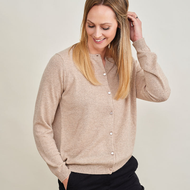 Woman wearing a beige cashmere cardigan against a plain background
