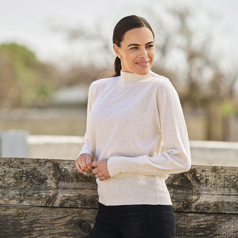 Woman wearing a cream cashmere sweater and black pants against a blurred background