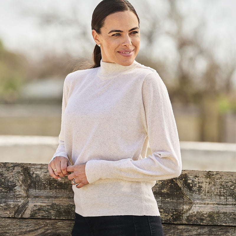 Woman wearing a cashmere cream sweater and beige pants against a blurred background