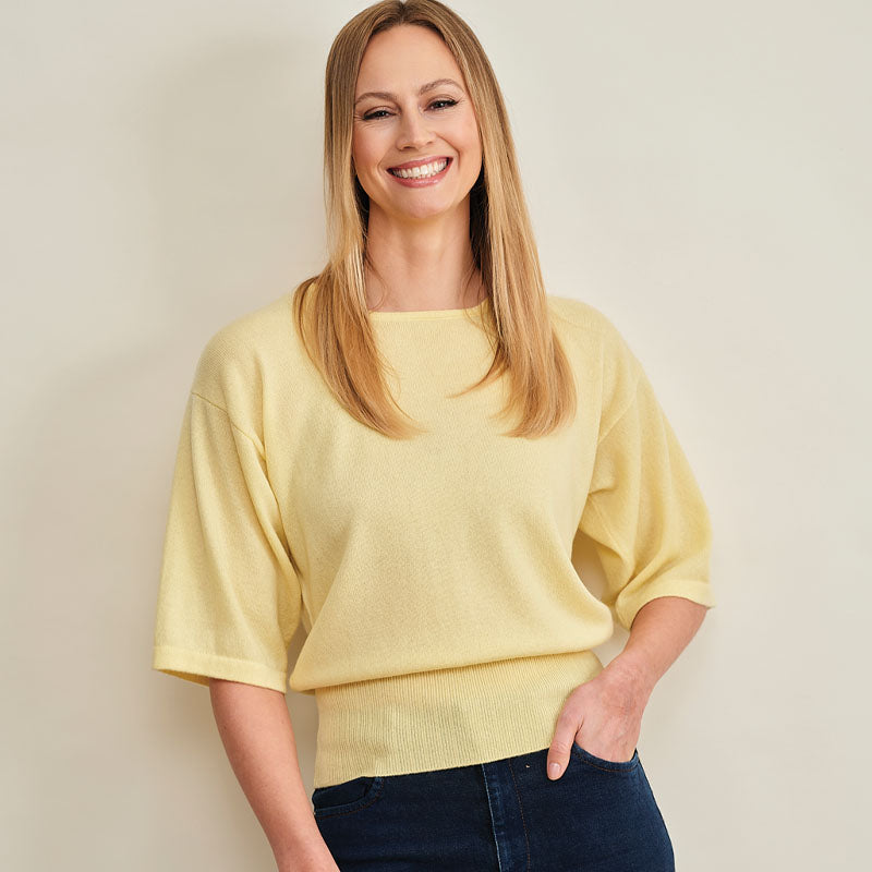 Woman wearing a yellow cashmere  sweater against a plain background