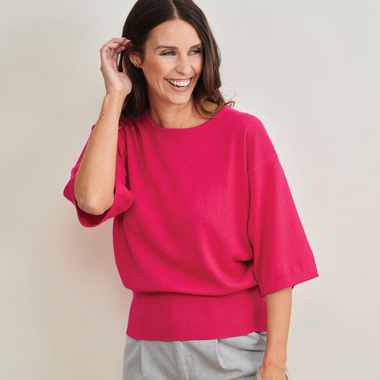 Woman wearing a  bright pink cashmere sweater against a plain background