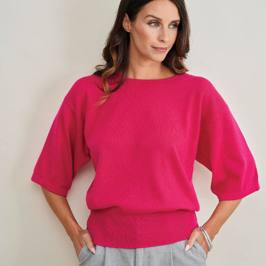 Woman wearing a Cashmere bright pink sweater against a plain background
