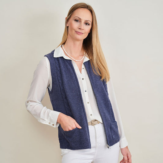 Woman wearing a blue cashmere vest over a white shirt with a beige background