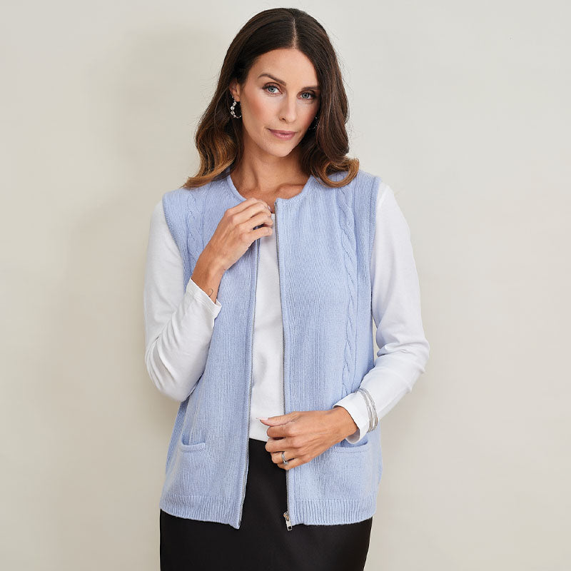 Woman wearing a light blue cashmere vest over a white shirt on a plain background