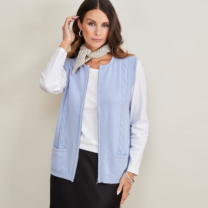 Woman wearing a cashmere  light blue cardigan over a white shirt with a beige background