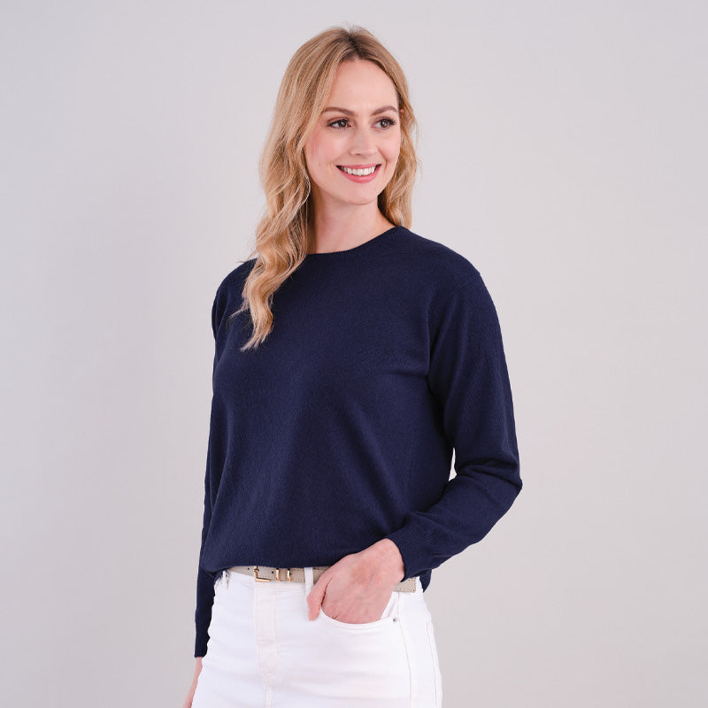 Woman wearing a cashmere hertiage sweater and white pants against a plain background