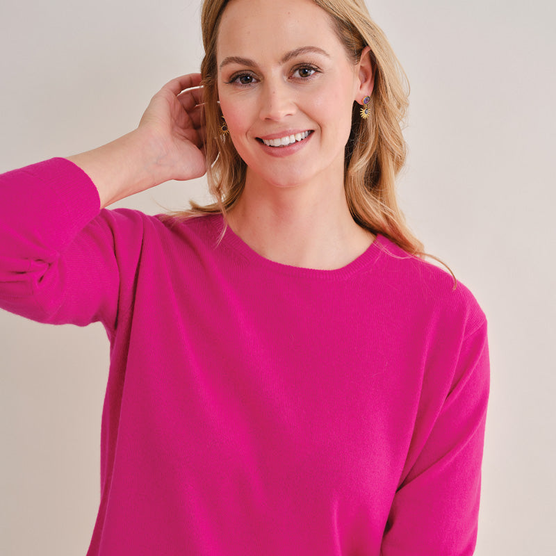 Woman wearing a Cashmere bright pink sweater against a plain background