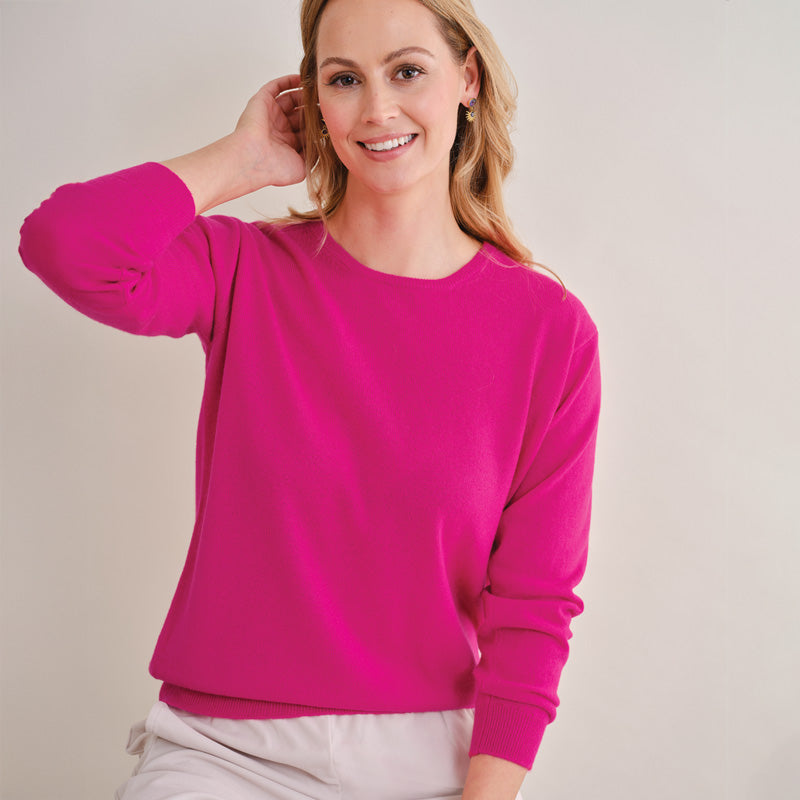 Woman wearing a cashmere bright pink sweatshirt against a plain background