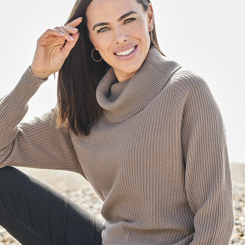 Woman wearing a cashmere beige turtleneck sweater sitting on a beach.