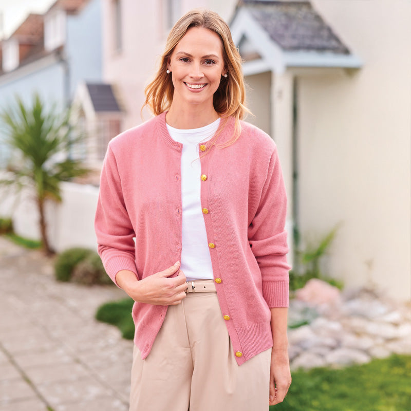 Woman wearing a  cashmere pink cardigan with gold buttons standing outdoors.