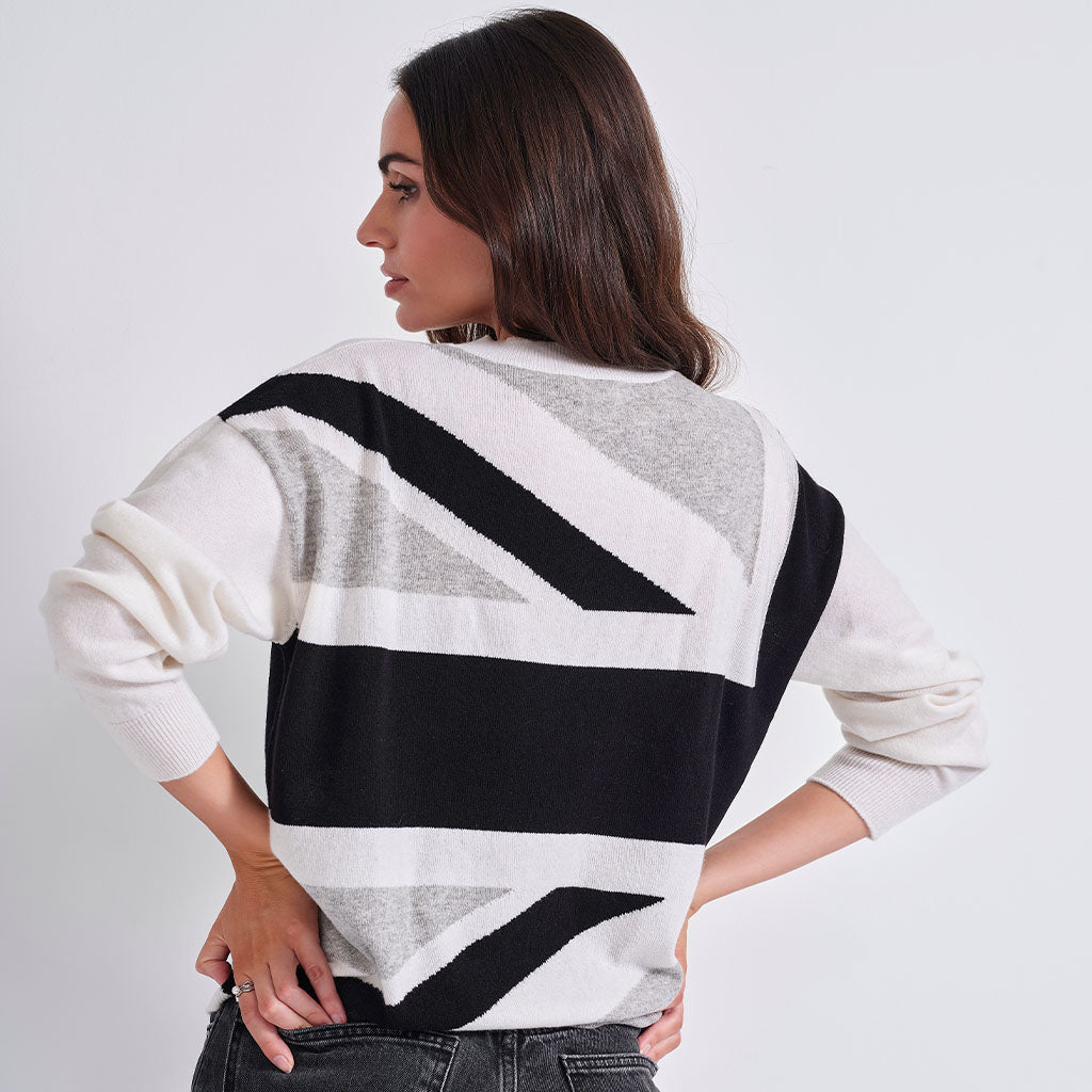 A woman wearing a knit sweater with a bold black, white, and gray geometric stripe pattern, shown from the back against a plain light gray studio background.