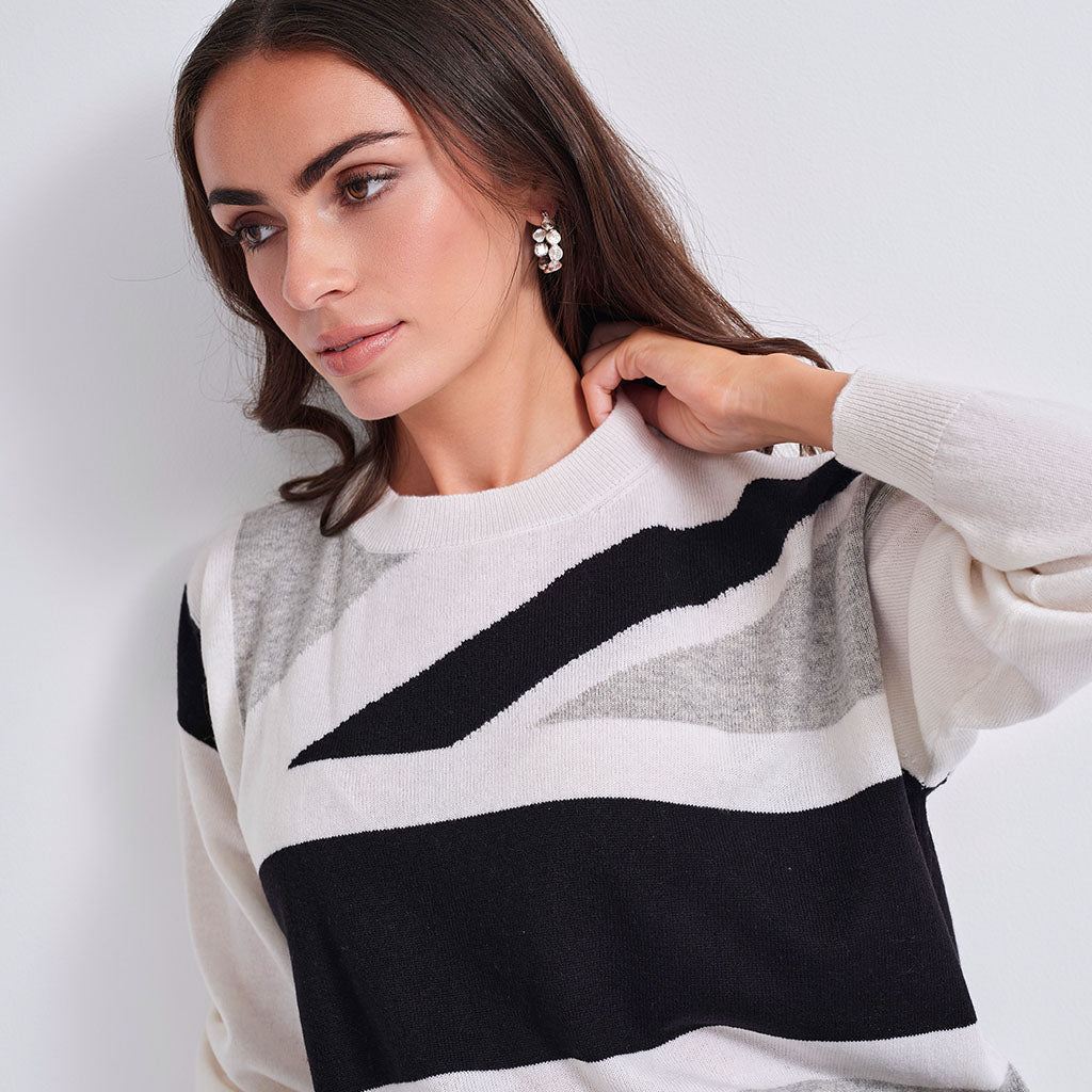 A woman wearing a knit sweater with a modern geometric color-block pattern in black, white, and gray, posed against a clean white background.