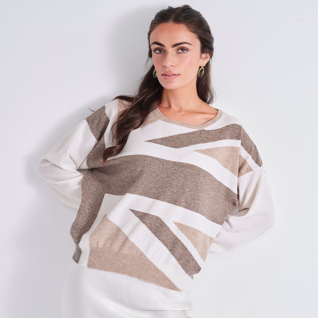 A woman modeling a long-sleeve knit sweater with a geometric stripe pattern in beige, taupe, and off-white, set against a plain light gray background.