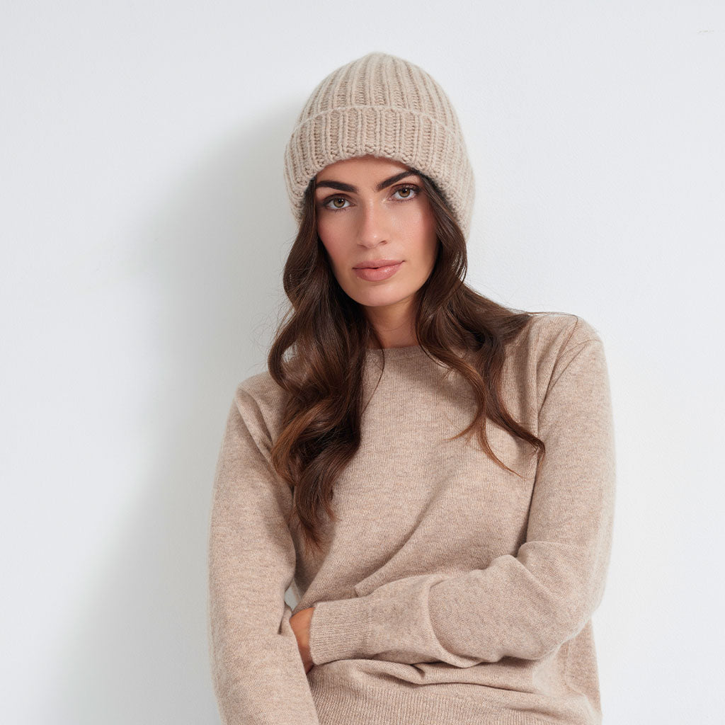 A woman wearing a beige ribbed knit beanie hat, shown in profile against a light gray background.