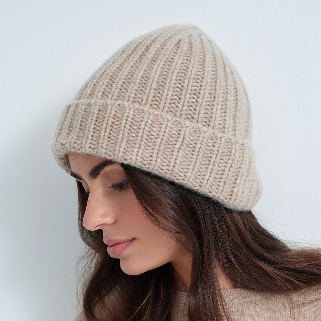A woman wearing a beige ribbed knit beanie hat, shown in profile against a light gray background.