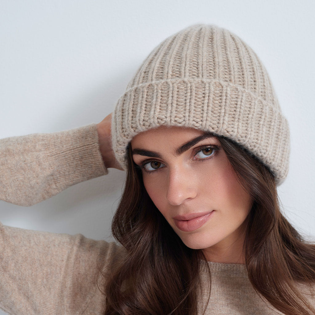 A woman wearing a beige ribbed knit beanie hat, shown in profile against a light gray background.