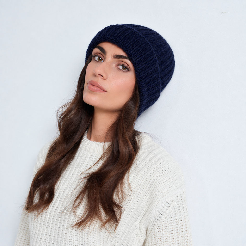 A woman wearing a dark navy blue ribbed knit beanie and a white knit sweater, photographed against a clean white background.