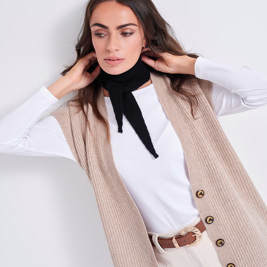 A woman wearing a beige ribbed button-front cardigan over a white long-sleeve top, with a black neck scarf and a brown belt, posed against a light gray studio background.