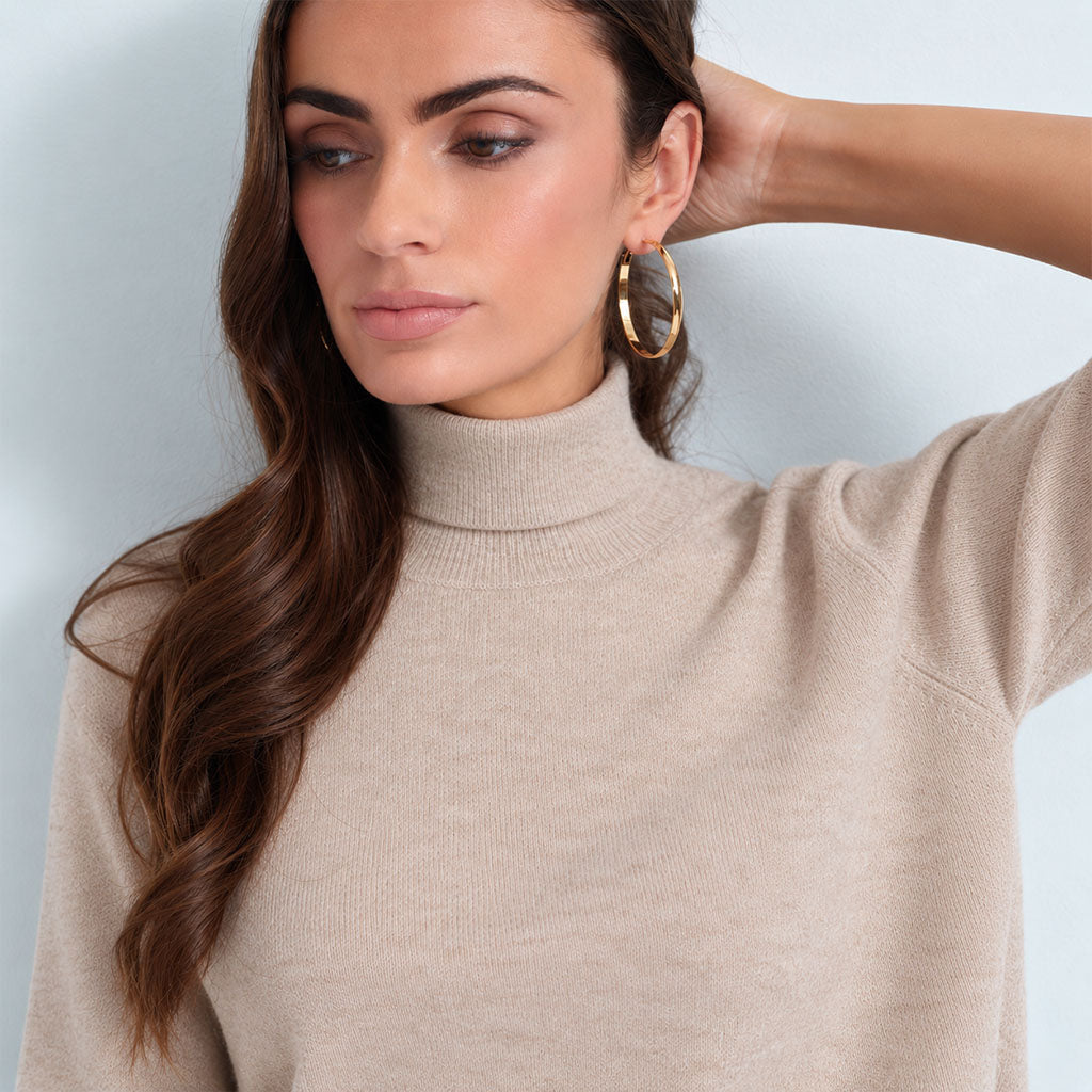 close up a woman modeling a beige short-sleeve mock neck knit top against a light blue-gray studio background.