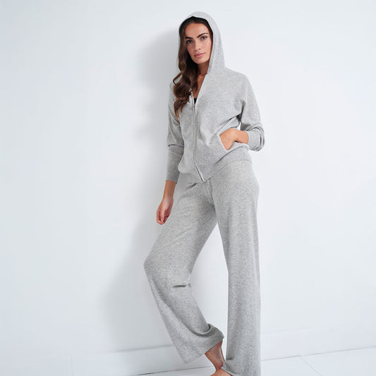 A woman modeling a light gray heathered zip-up hoodie and matching wide-leg sweatpants set against a plain white studio background.