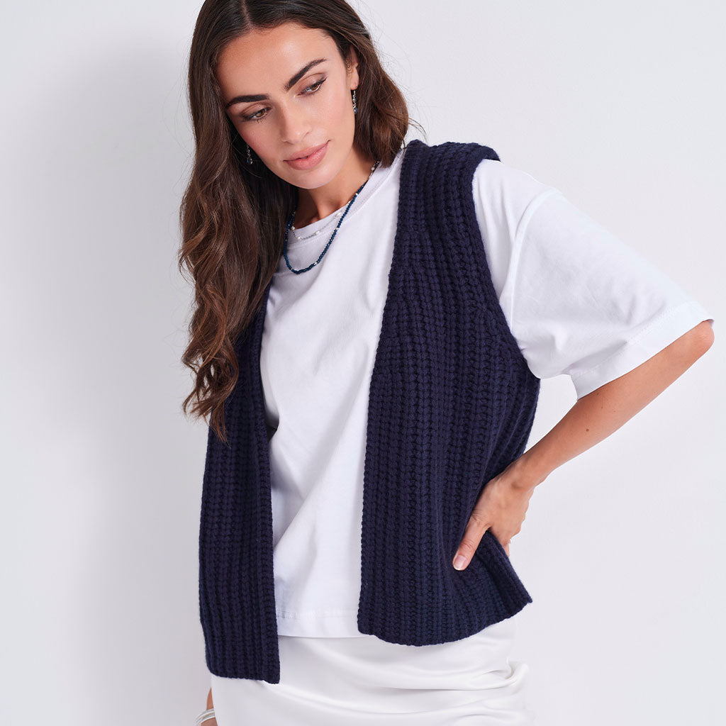 A woman wearing a navy blue ribbed knit sleeveless vest over a white t-shirt, photographed against a clean white studio background.