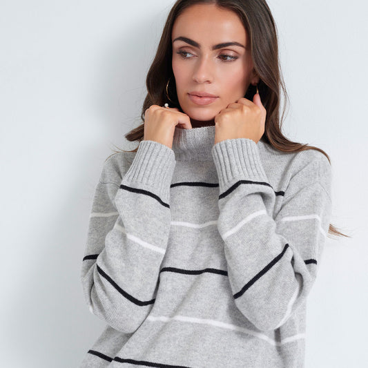 A woman wearing a light gray knit sweater with horizontal black and white stripes, posing against a light gray background.