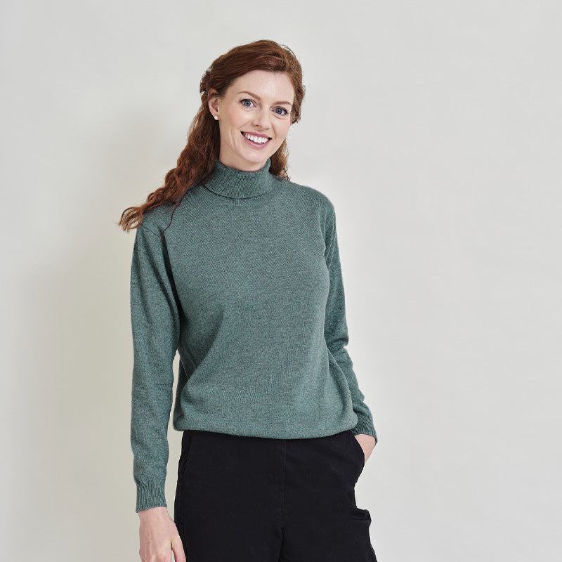 Woman wearing a cashmere green turtleneck sweater against a plain background
