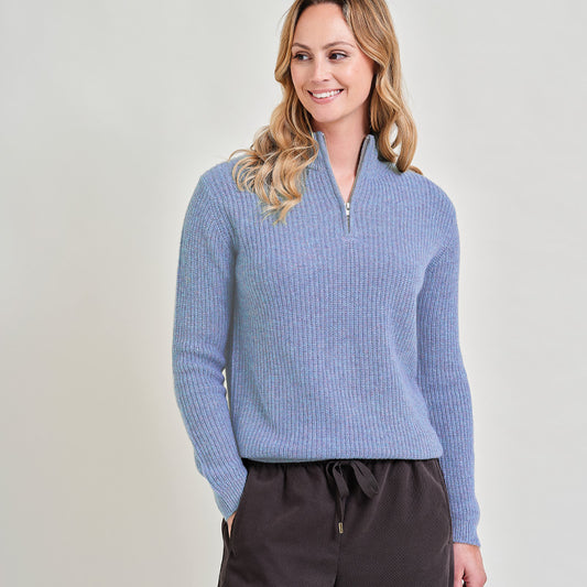 Woman wearing a cashmere denim blue ribbed sweater with a zipper on a light gray background