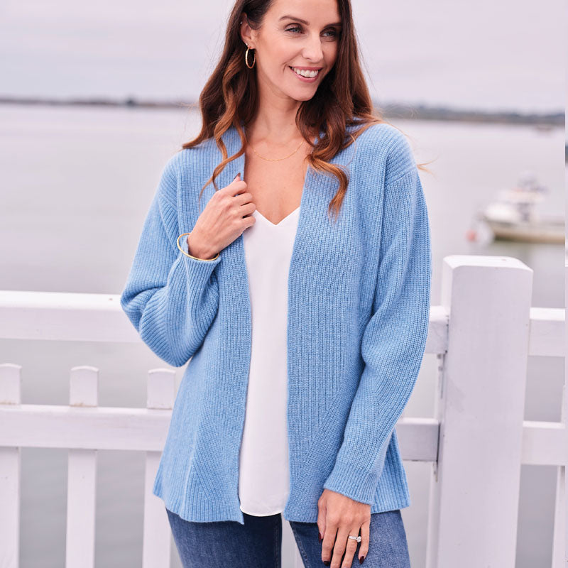 Woman wearing a light blue cashmere cardigan over a white top, standing on a dock.